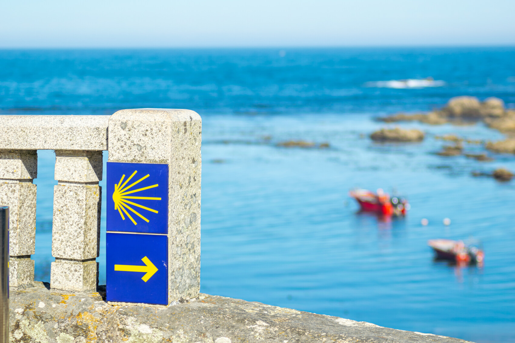 A route marker with the sea behind it on the Camino de Santiago