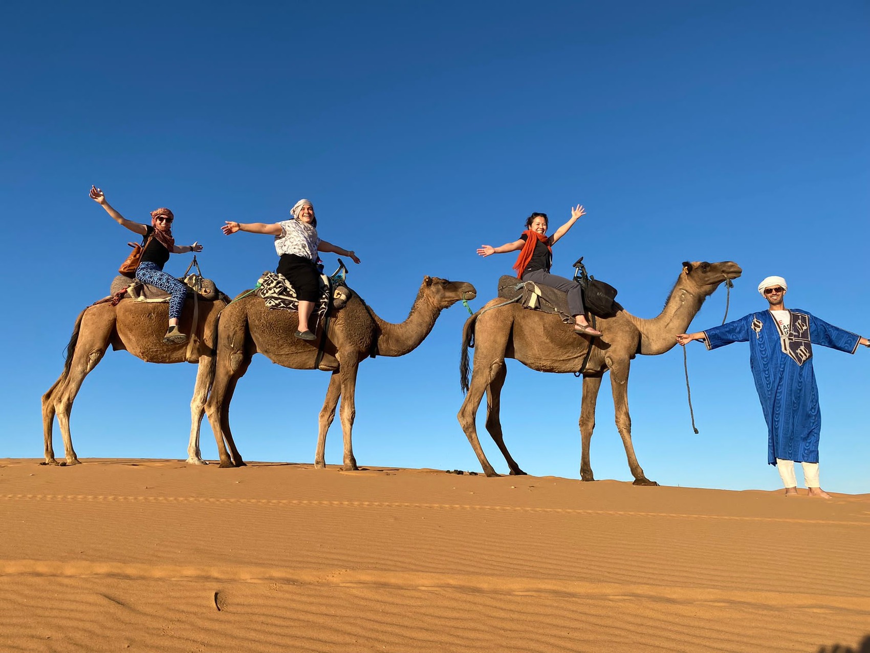 A group of travellers waving from camels in the Sahara Desert