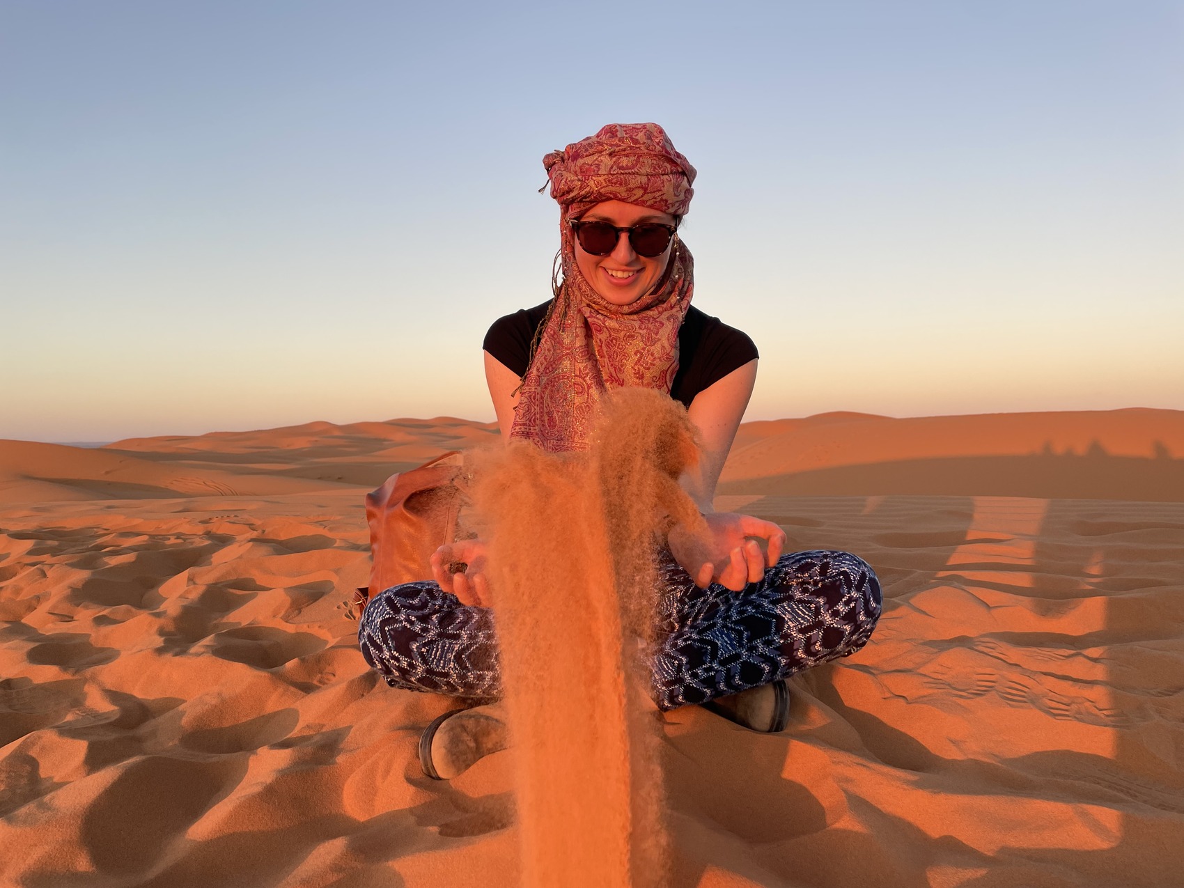 Lydia sitting in the desert in Morocco playing with sand