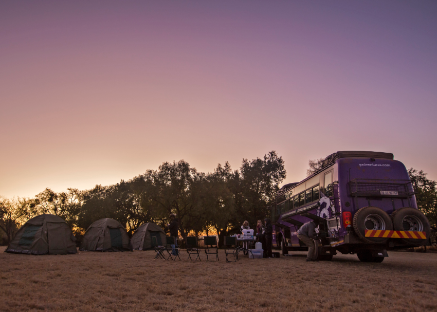 G Adventures travellers set up camp as the sky turns as purple as our overland safari vehicle